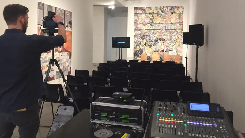 Osoba ustawiająca sprzęt audiowizualny w pokoju z miejscami do siedzenia i dziełami sztuki na ścianach.