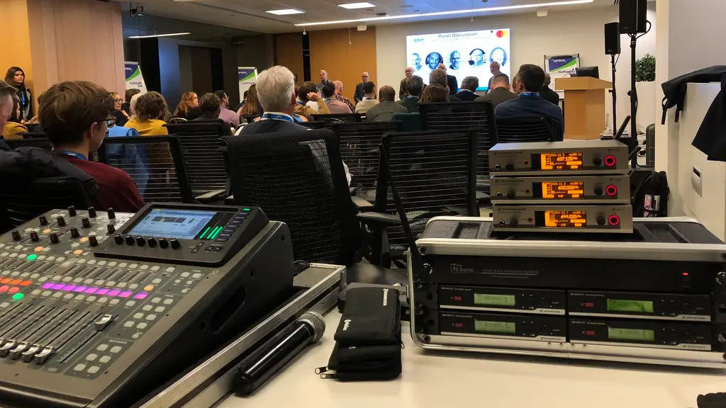 Sala konferencyjna z wyposażeniem audiowizualnym i publicznością słuchającą prezentacji.