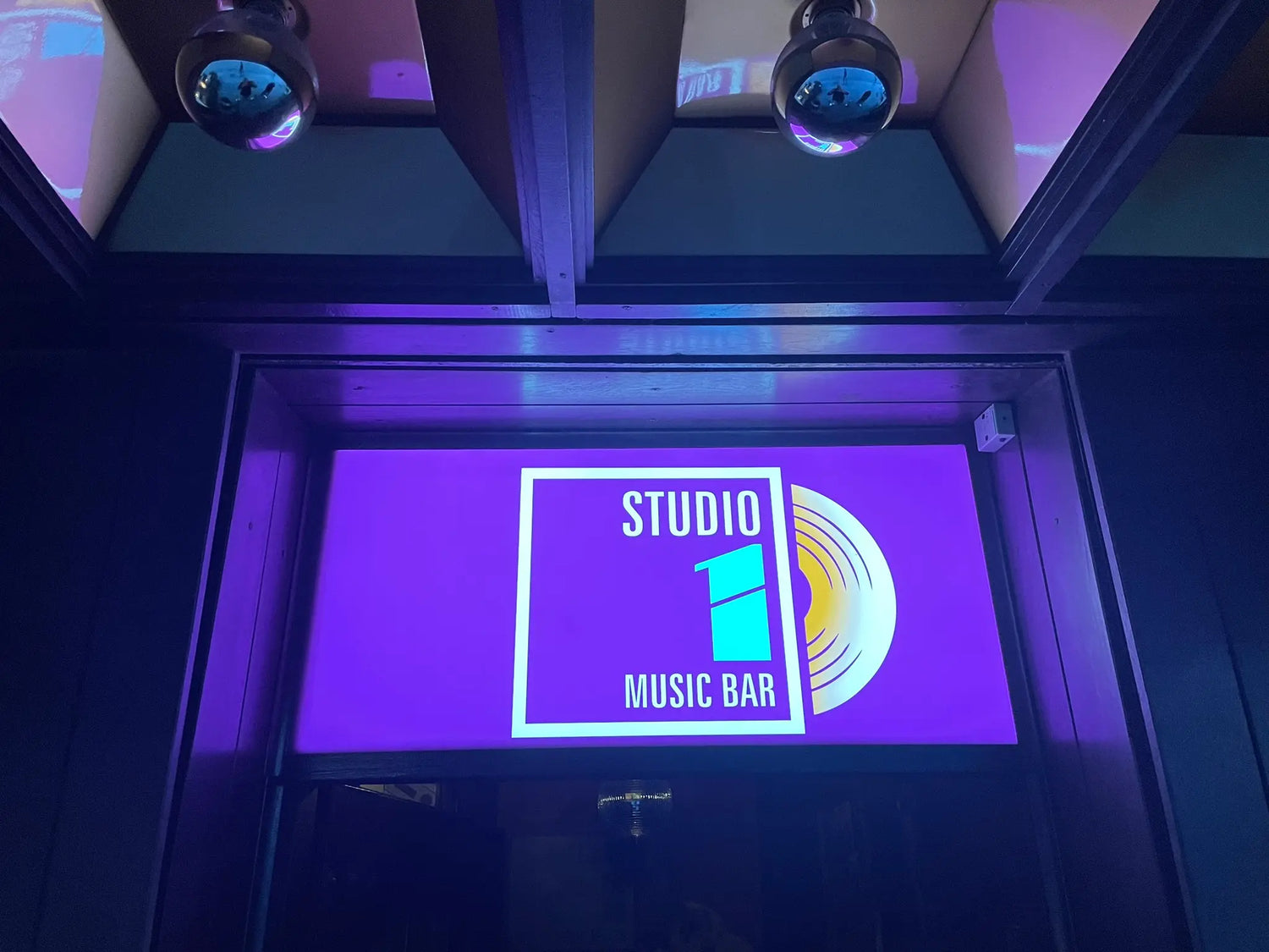 Fioletowe wnętrze baru muzycznego z wyświetlonym na ścianie napisem 'Studio Music Bar'.